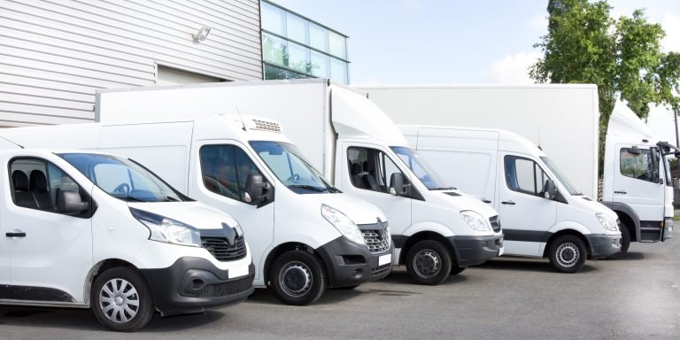 Several cars vans trucks parked in parking lot for rent or delivery